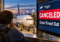 Traveler at an airport after a flight is canceled because the crew timed out, with an aircraft at the gate and a cancellation notice on the departure board.