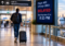 Traveler leaving an airport terminal during a long flight delay while a departure board shows a revised departure time.